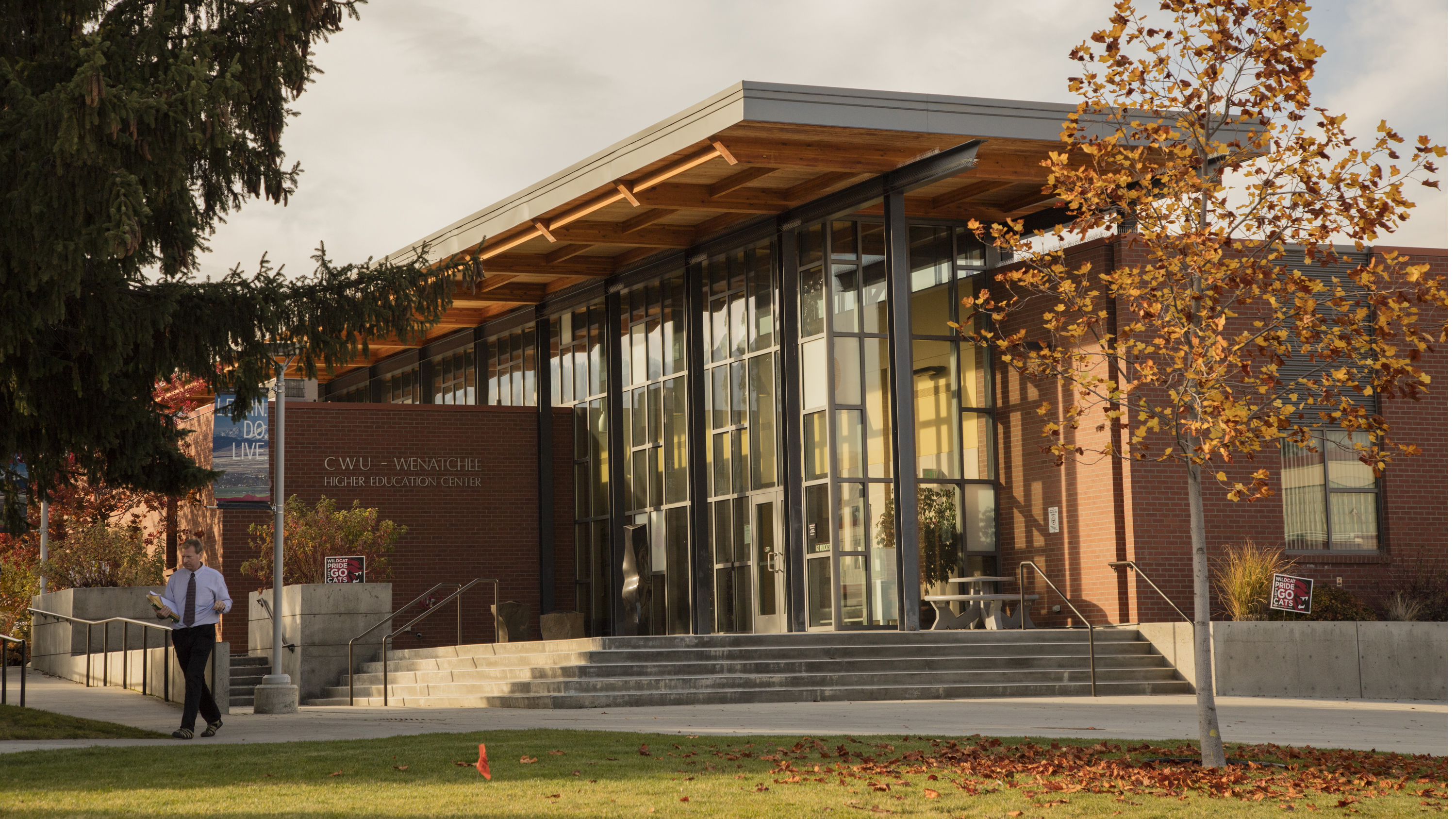 CWU Wenatchee building. It has a lot of windows and there are stairs leading to the entrance. There is a man outside of the building wearing slacks, a button-up, and a tie.