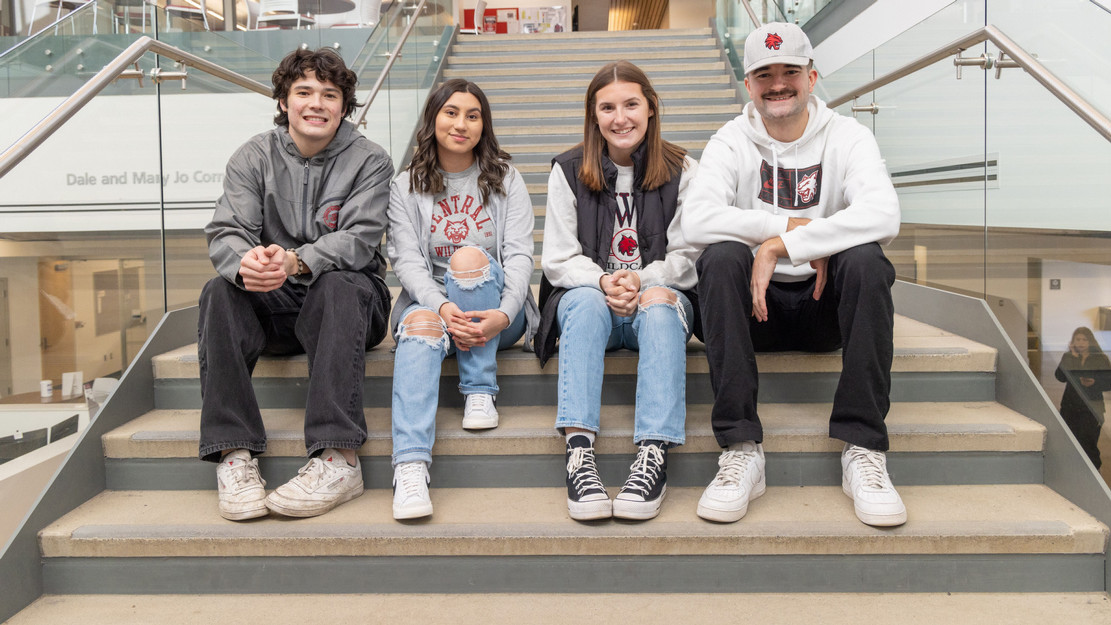 Four students in CWU sweaters smiling and sitting on steps