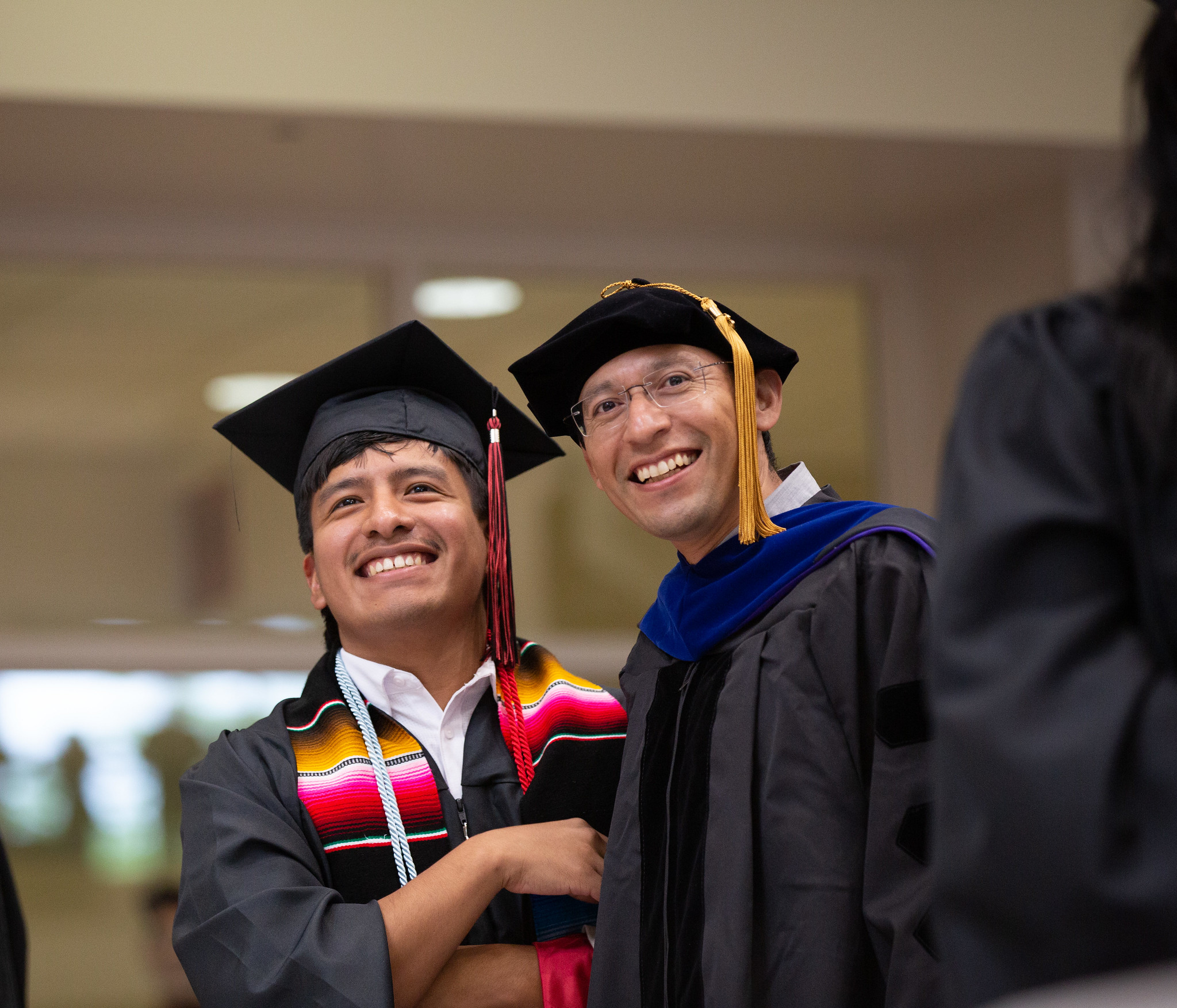 Student and professor smiling together at commencement ceremony.