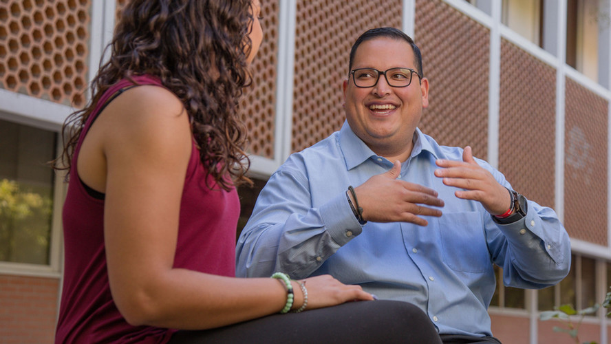 A man within the hep program at Central Washington University sits down with a student and engages in conversation.