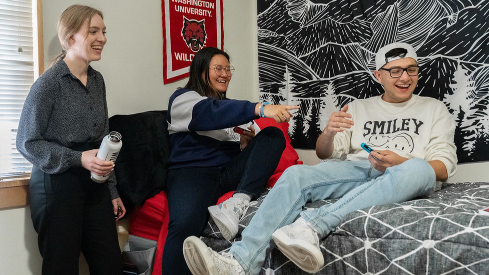 Three students at Central Washington University sit on bed within the dorms and share a laugh.
