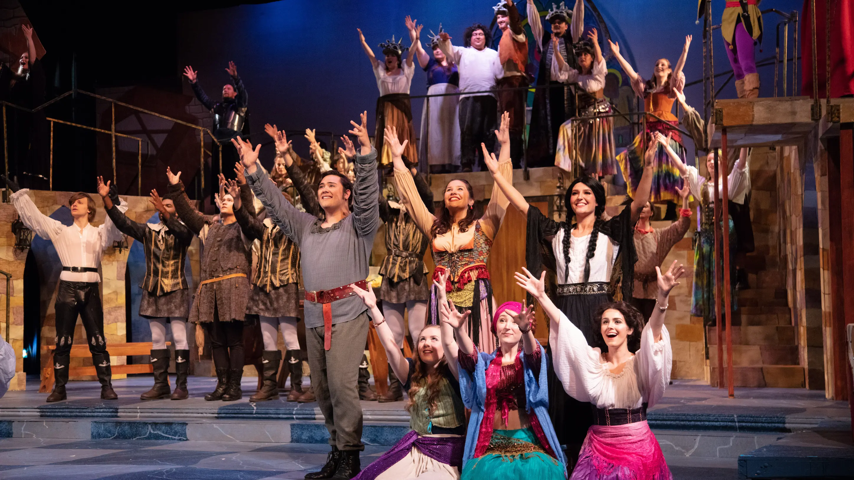 Group of students in costume on stage acting, extending both their arms outward 