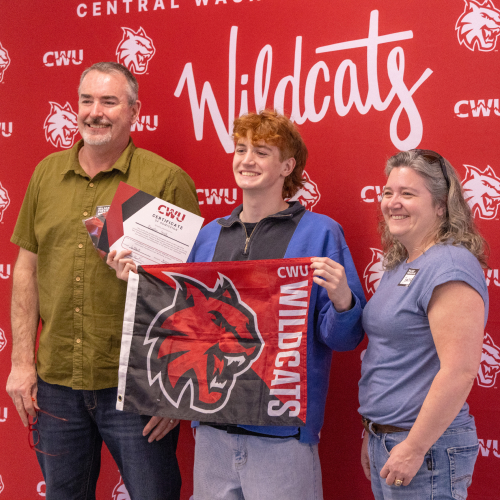 Incoming student holding up a CWU flag and standing with their parents.