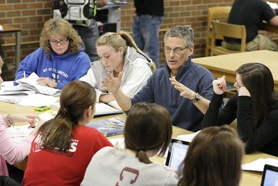 Professor lecturing to students seated around a table..
