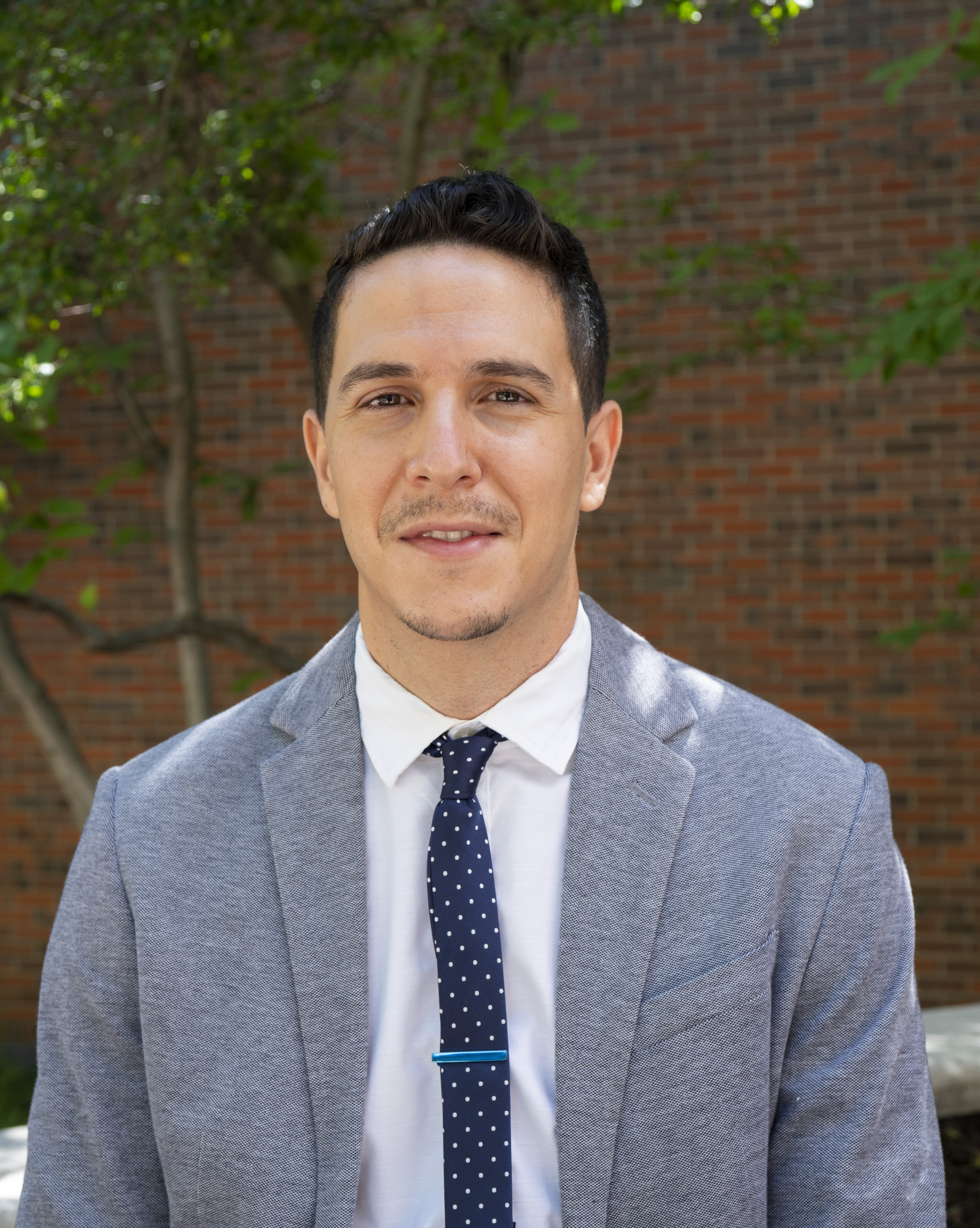 Headshot of the art historian Asiel Sepulveda, a Latinx man wearing a light blue suit and blue polka dot tie.