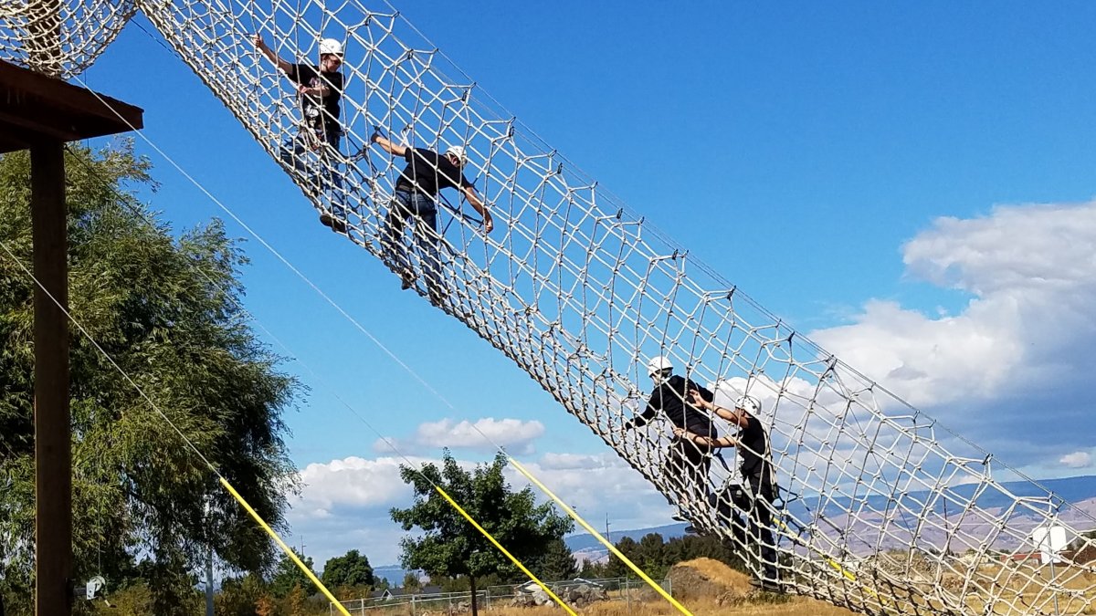 Four CWU students climbing up a rope ladder.