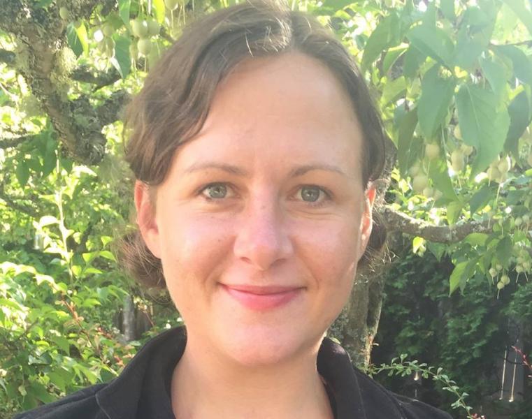 Sonya Dunning grinning with greenery behind her and a black collared shirt