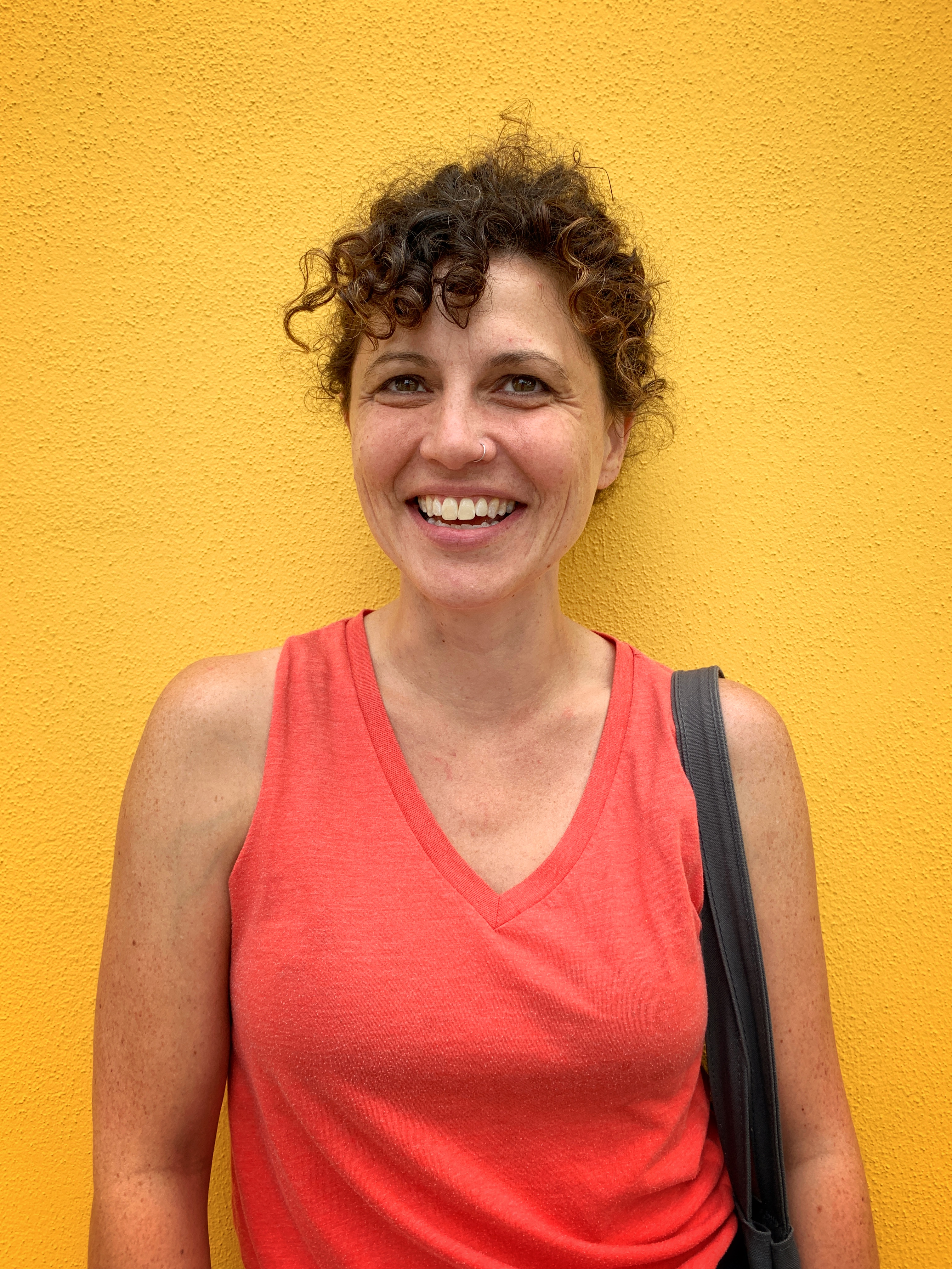 Headshot of Elaina Ellis against a yellow wall, smiling and looking at the camera wearing an orange tanktop.