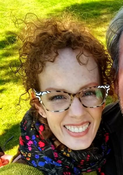Photo of Janelle Serio smiling while wearing multicolor glasses and scarf