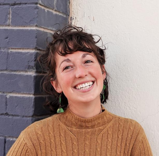 Portrait of Gianna Starble wearing a gold sweater and statement earrings, smiling at the camera