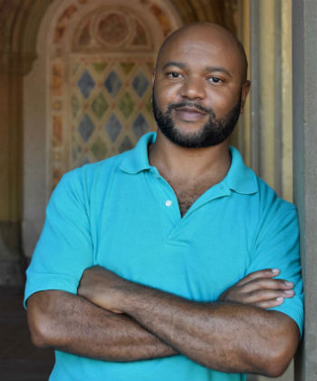 Portrait of De'Shawn Charles Winslow with crossed arms wearing a blue collared shirt