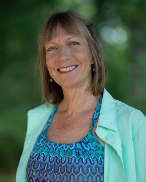 Lisa Norris smiling with greenery behind her in a teal and mint layered tops