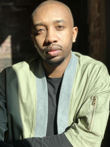 Portrait of Luther Hughes staring into the camera wearing tan and gray shirt