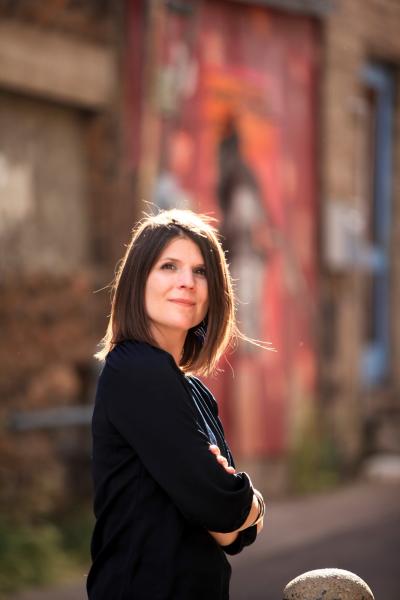 Erin Stalcup looking up with tall buildings behind her with the sun like a halo in her hair 