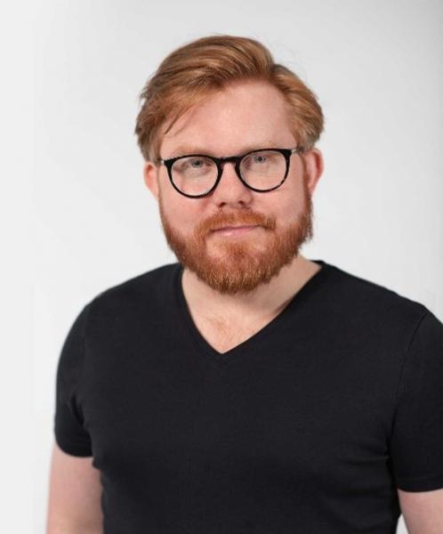 Portrait of Taylor Brorby looking at the camera wearing black glasses and black t-shirt