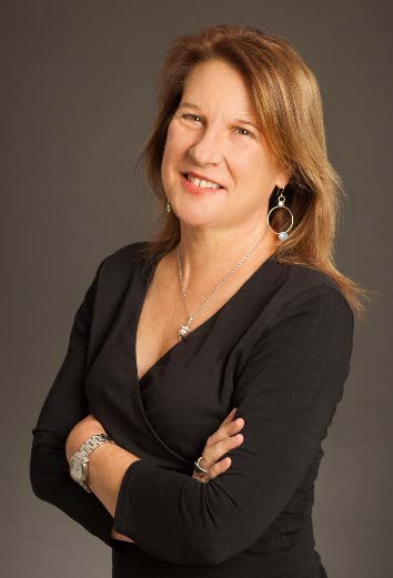 Katharine Whitcomb smiling in a black top with dangly earrings
