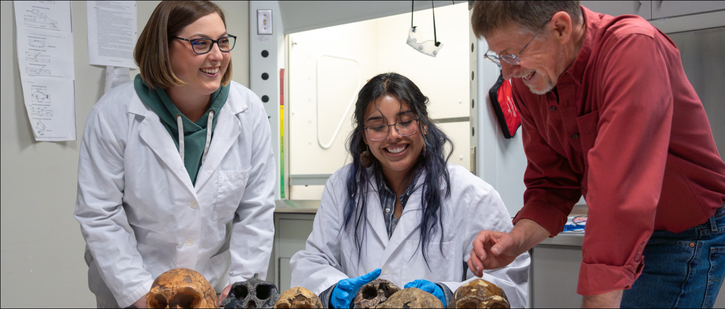 Two professors working with a student in an anthropology lab examining skulls