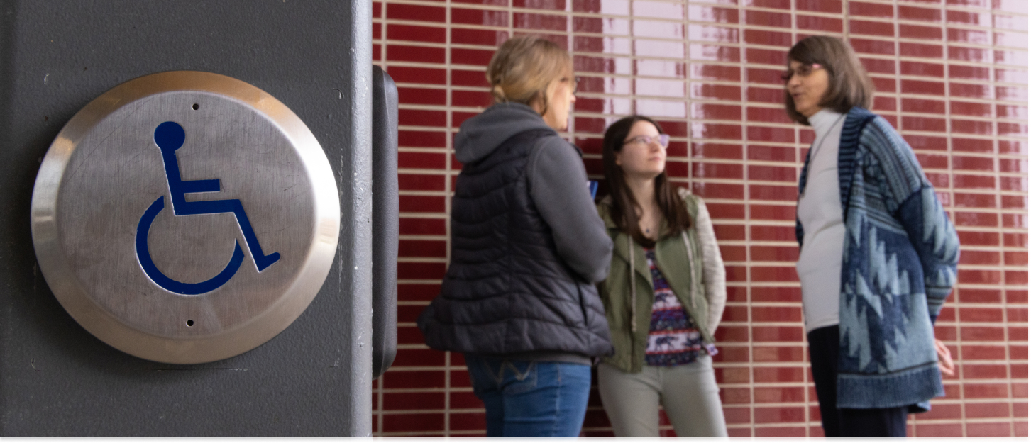 Photo of an accessibility button to open a door with students and specialist talking behind it