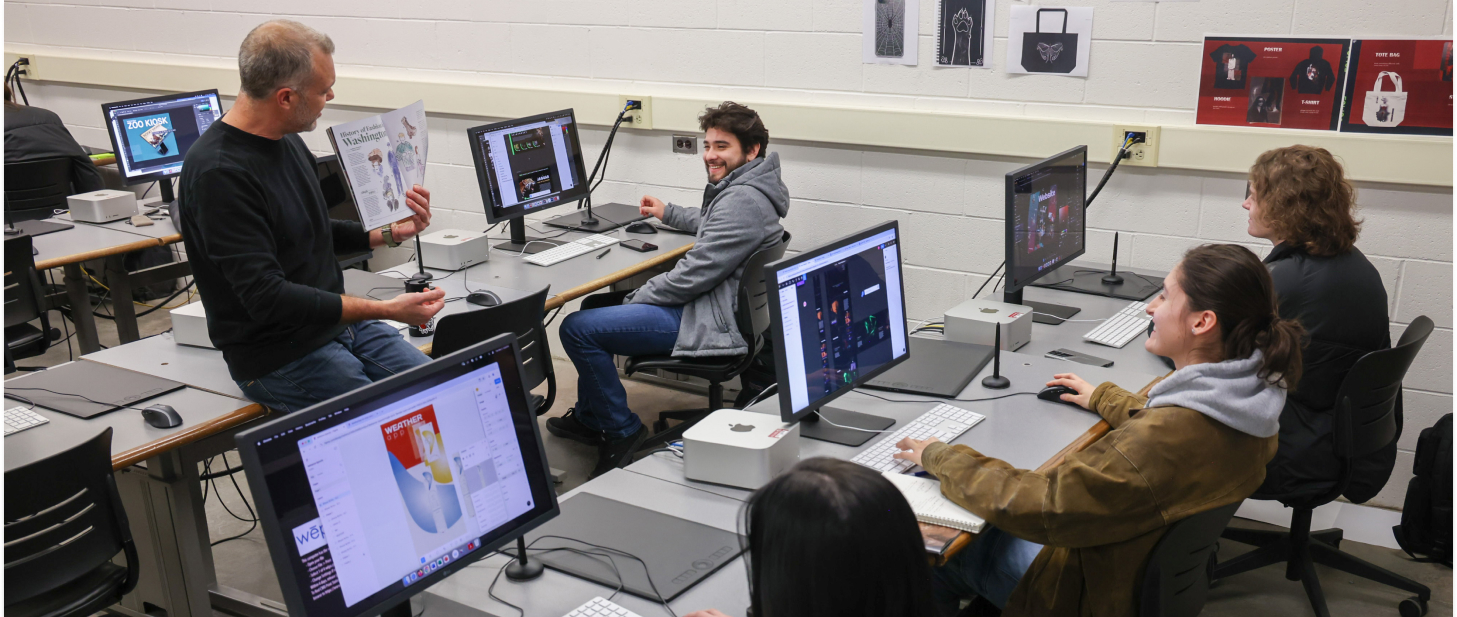 Students in the classroom looking at the professor going over design features of a magazine.