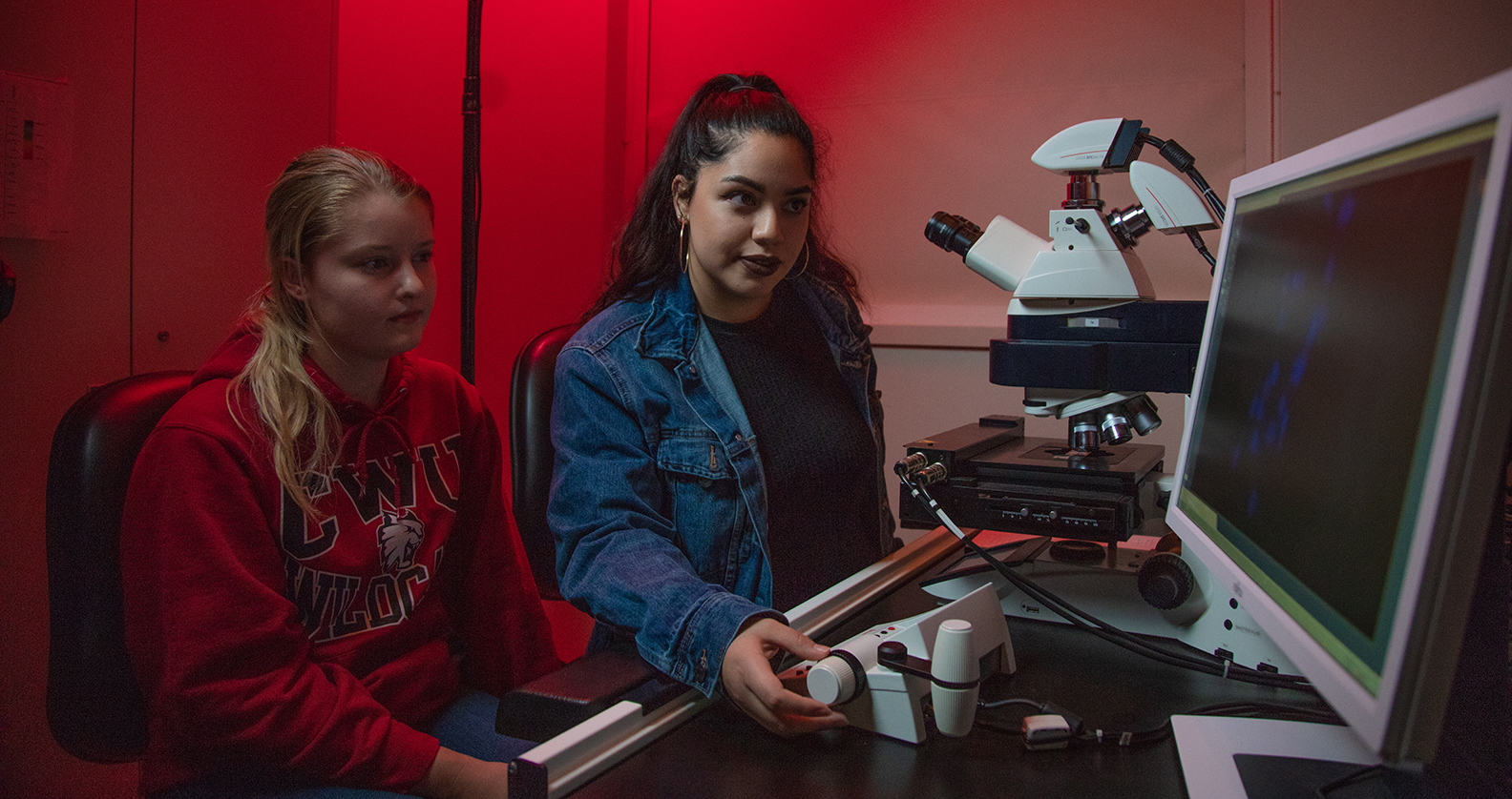 Two students in a red room looking at a computer