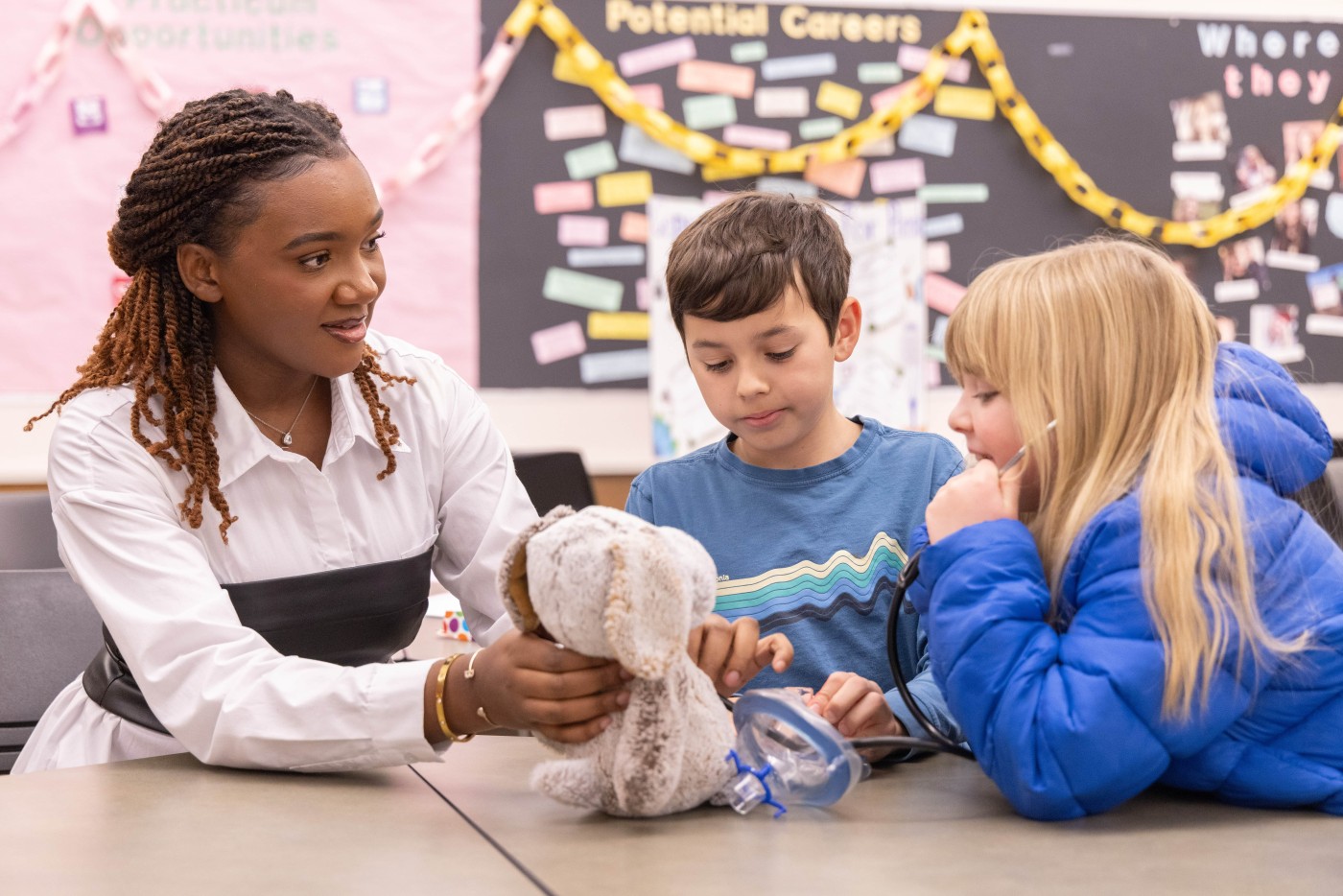 Student holding stuffed animal while child listens to heartbeat with a stethascope