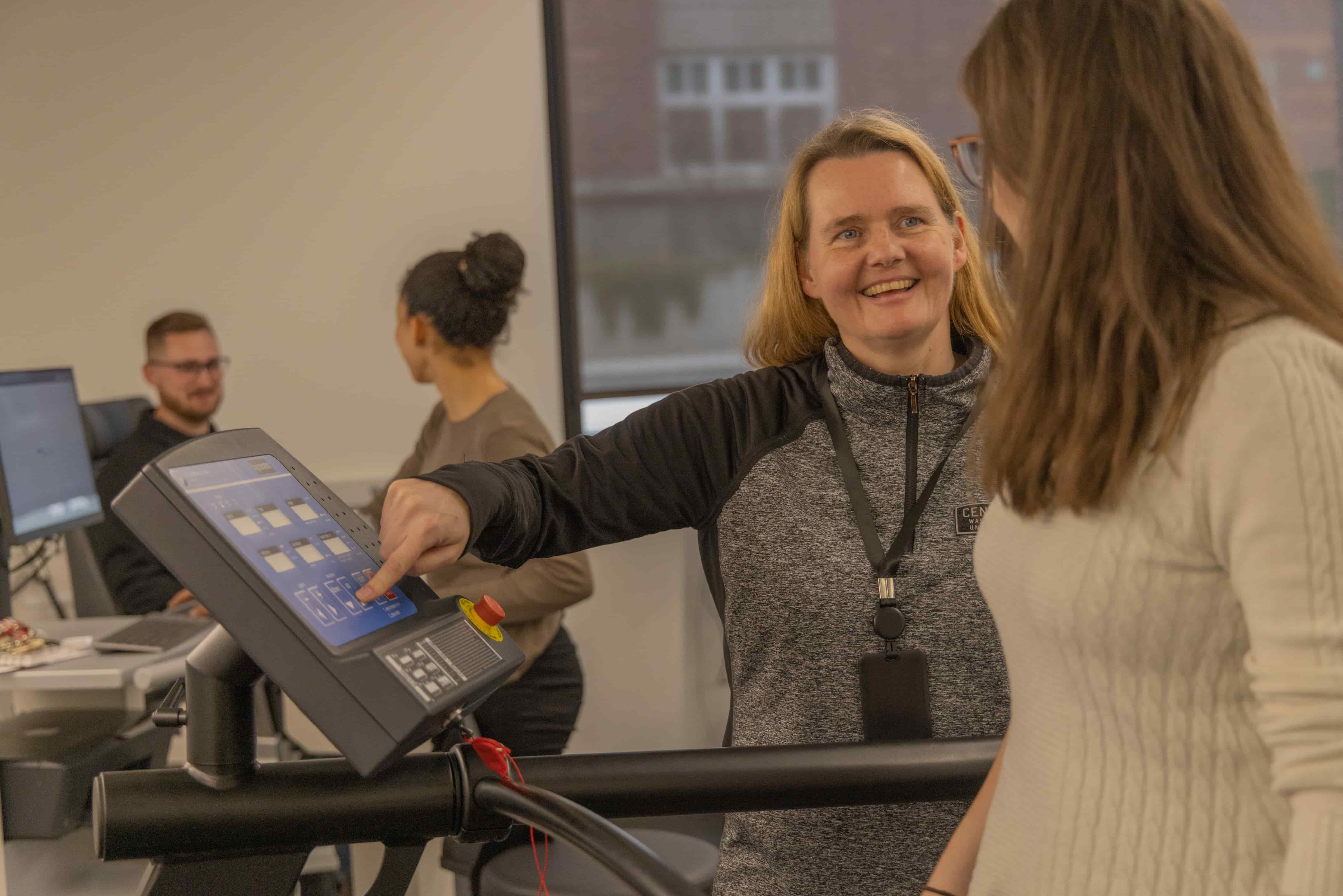 A CWU professor assists a student using exercise equipment.