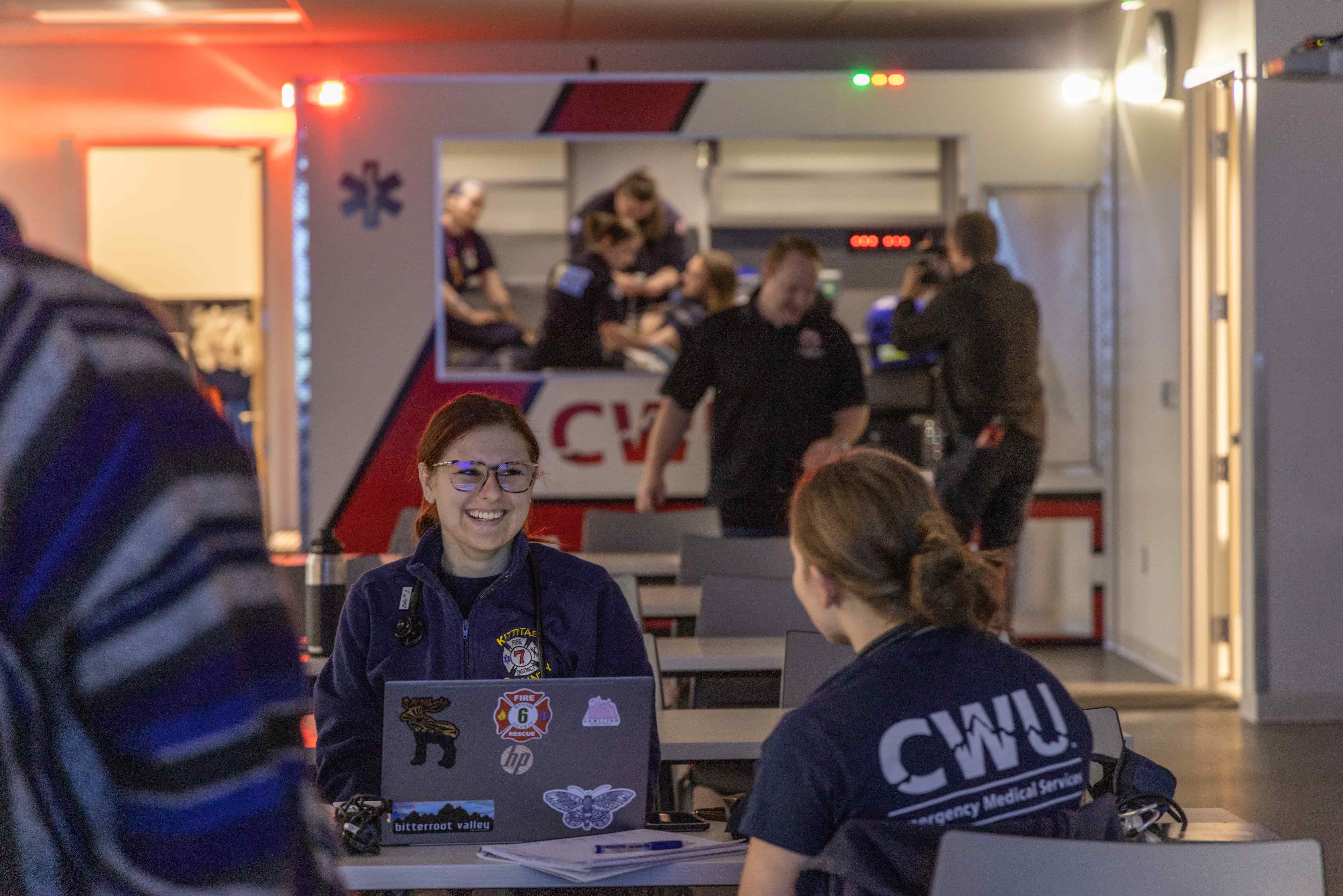 CWU EMS students in a class. One sits on a laptop smiling to a classmate.