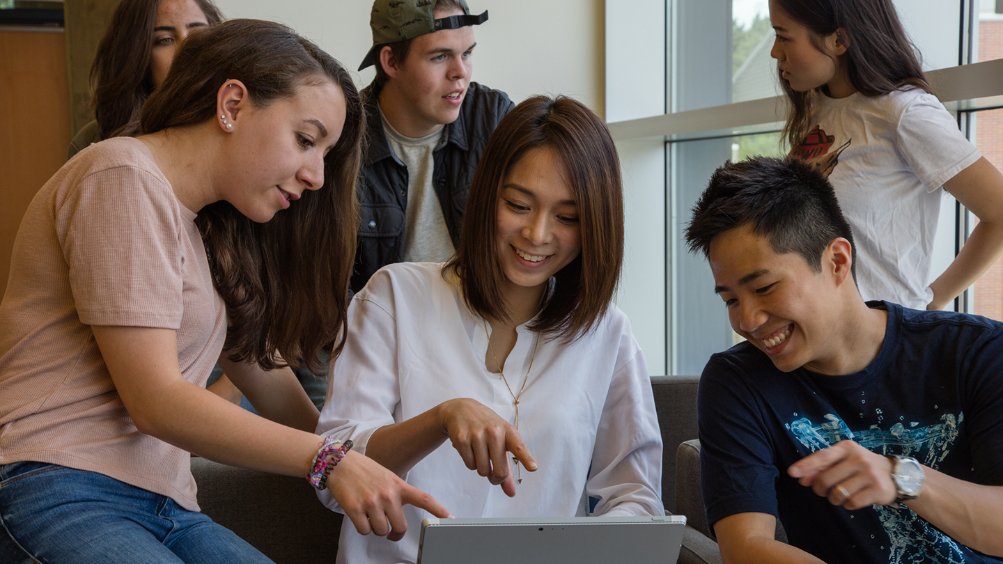 a group of students smilling and pointing at a laptop