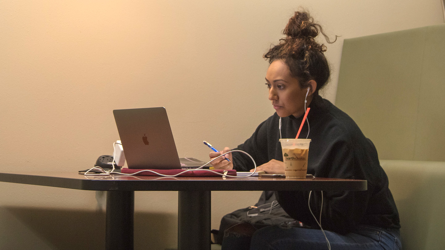 a student reading from her laptop while holding a pen