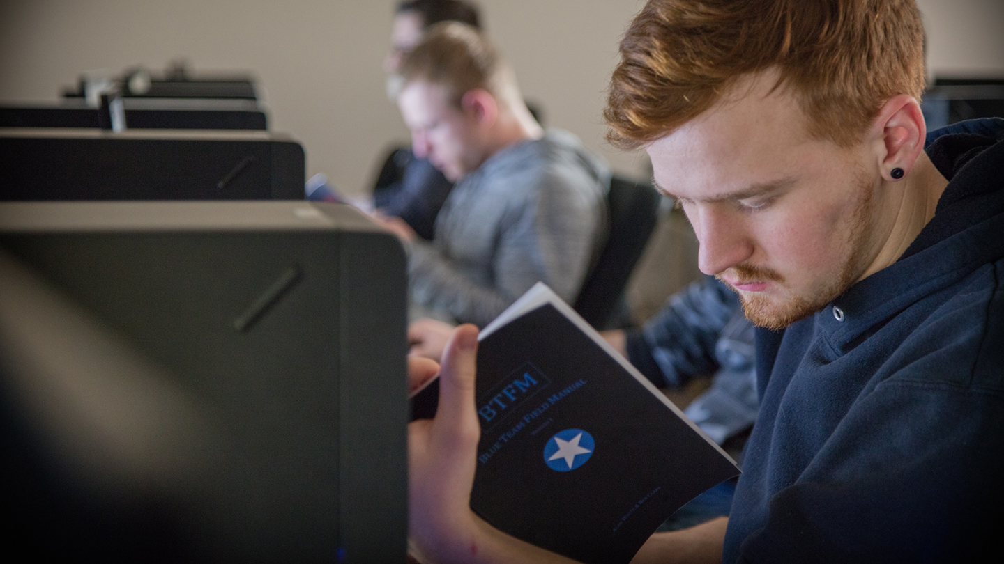 Student writing in a notebook in a computer lab.