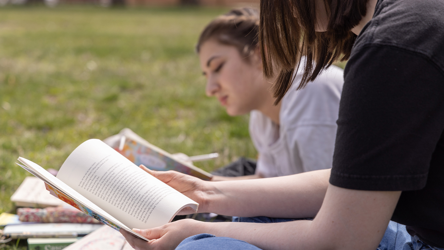 Two students reading a book in the grass. 