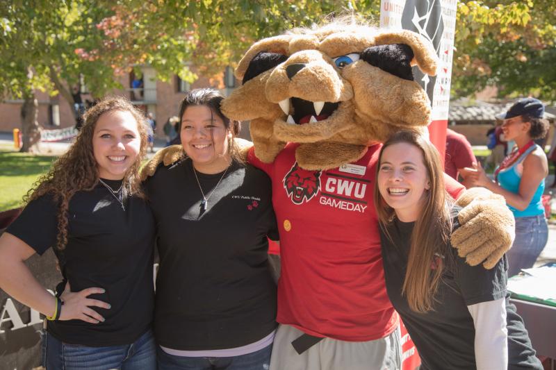 Three students smiling with CWU mascot, Wellington Wildcat