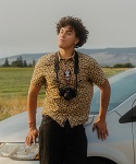 Roberto Chavez leaning against a car. He has a camera hanging from his neck