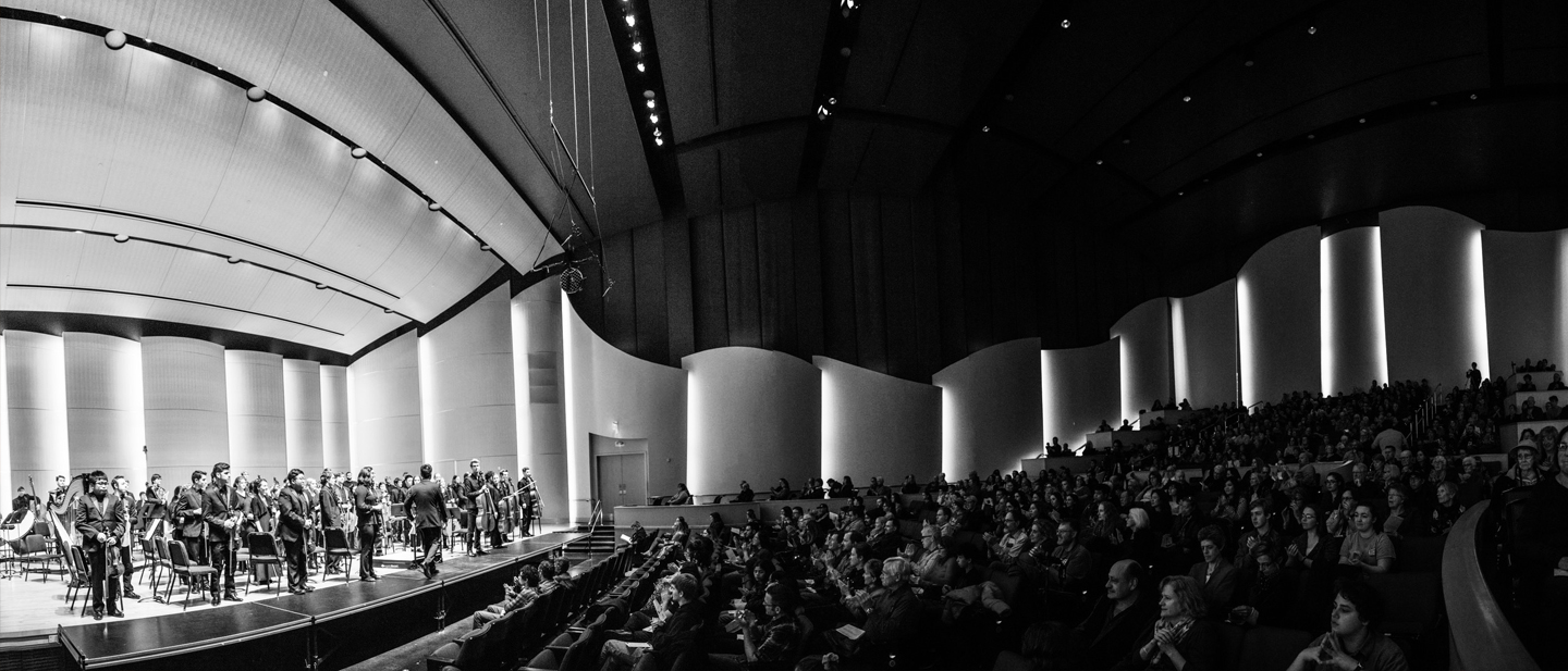 Wide angle black and white image from the side view of CWU orchestra performing to a full house.