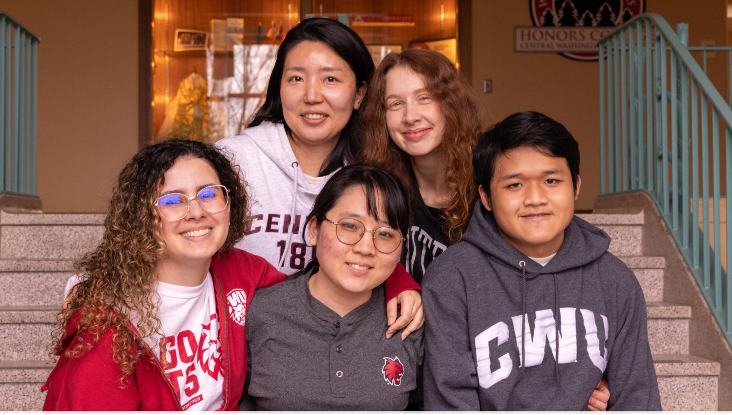 Five students wearing CWU branded sweaters, smiling while sitting on stairs.