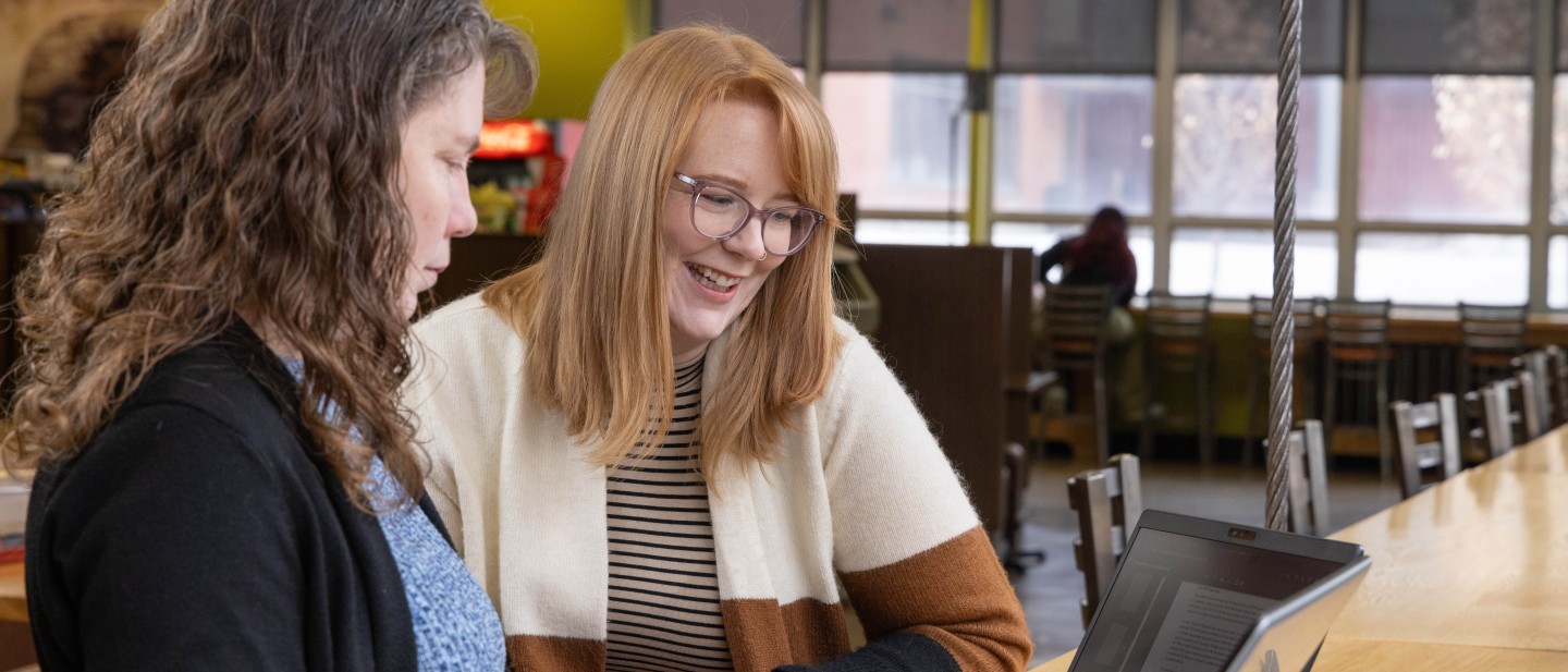 TWo students looking at a laptop at a cafe on campus.